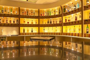 Zona de bar con varias estanterías llenas de botellas de licor, una barra central y un suelo pulido y reflectante.