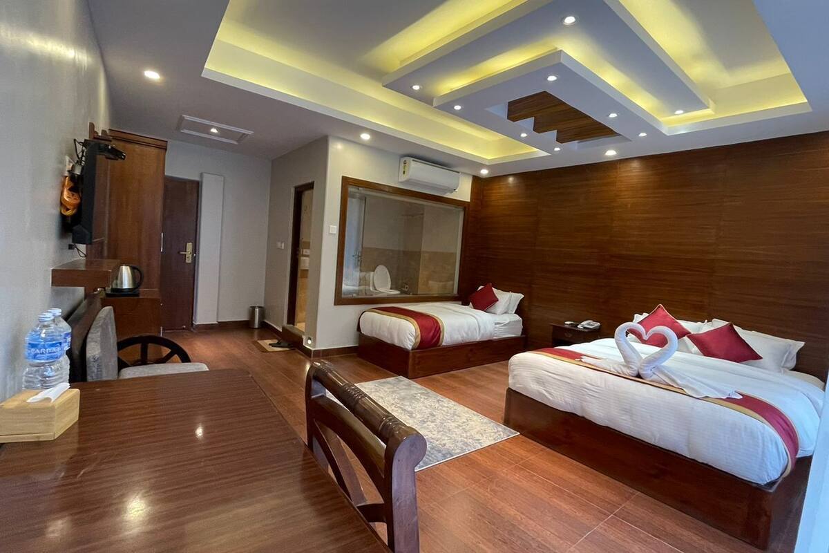 Una habitación de hotel con dos camas, suelo de madera, una mesa de comedor y un espejo grande.