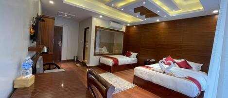 A hotel room with two beds, a wooden floor, a dining table, and a large mirror.