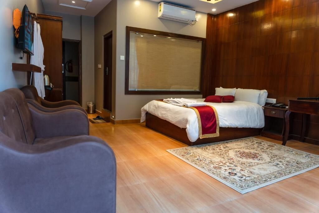 A hotel room with a bed, a sofa, a wooden floor, and a large window.