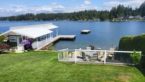 A lakeside property with a dock, a covered outdoor seating area, and a view of the lake and forested hills. - Lakefront House with dock and lots of toys! (Stanwood)
