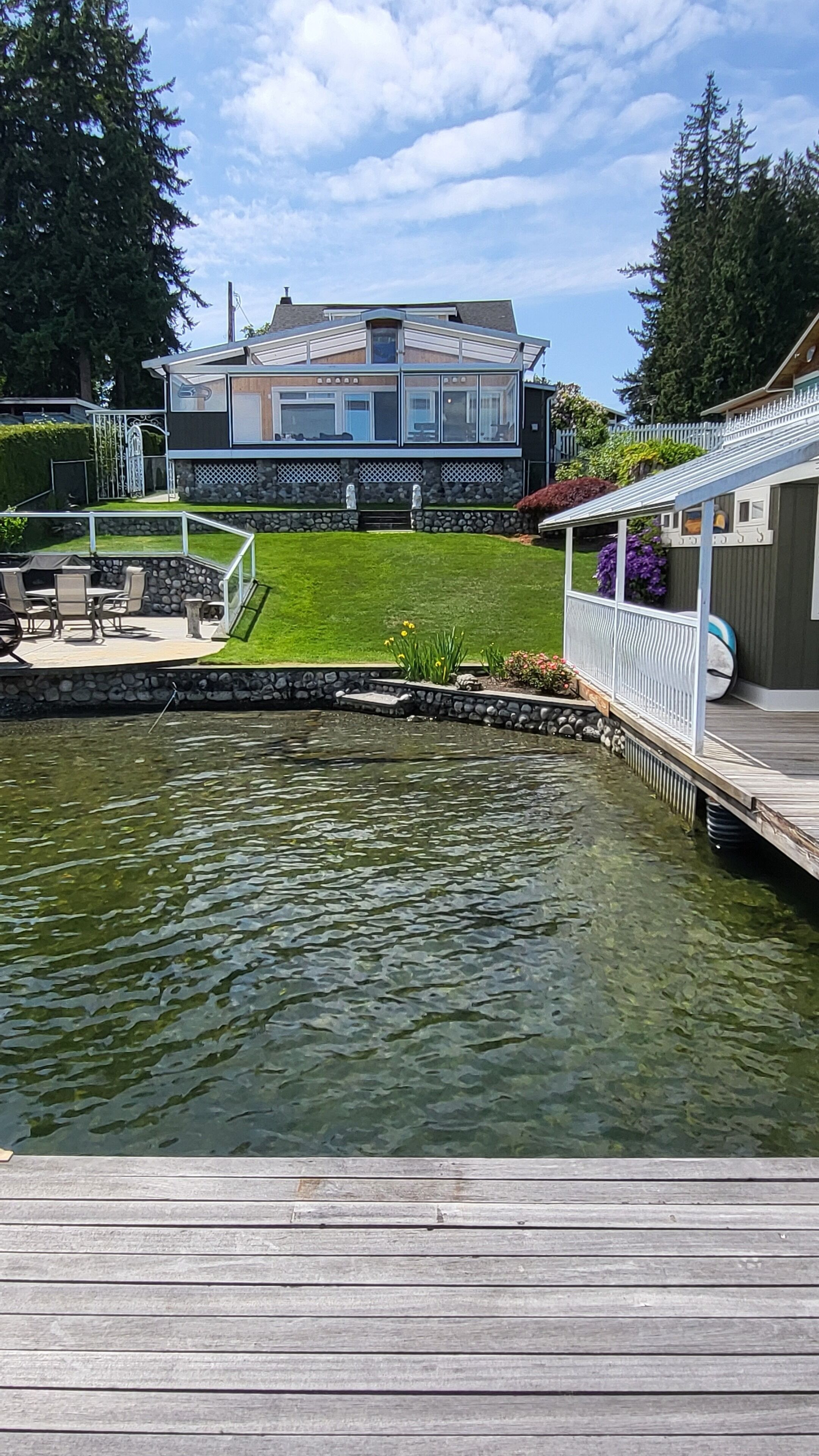 A house with a stone foundation, a wooden deck, and a small pond.