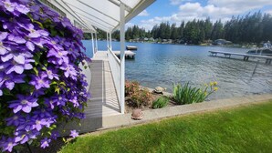 A lakeside deck with a view of a lake, surrounded by greenery and houses in the background. - Lakefront House with dock and lots of toys! (Stanwood)