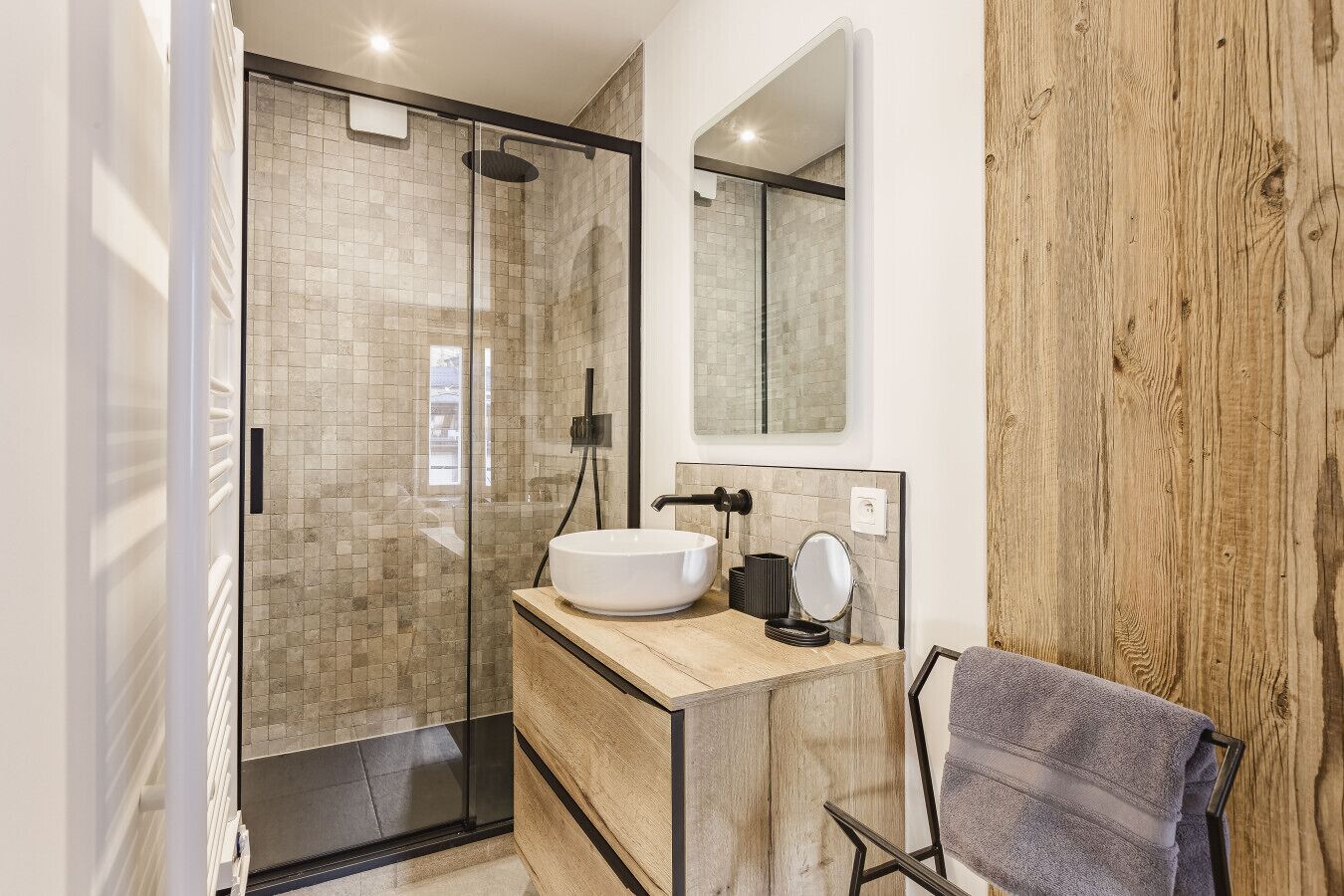 A modern bathroom with a glass-enclosed shower, a wooden vanity, and a large mirror.