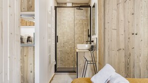 Een moderne badkamer met een douchecabine van glas, een wit wastafeltje en een houten vloer.