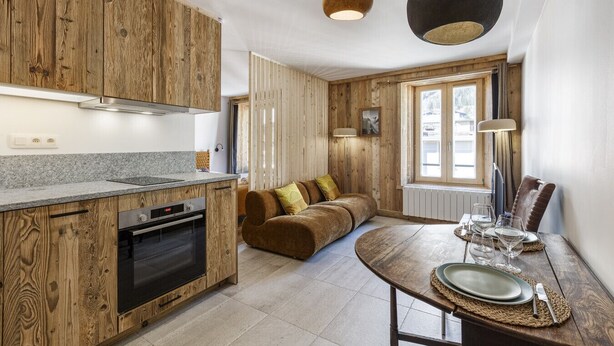 Een moderne keuken met houten kastjes, een ingebouwde oven en een eethoek met een ronde tafel gedekt voor twee personen.