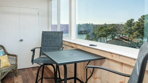 A balcony with a table and chairs, a wicker chair, and a view of a landscape with trees and a bridge. - Lakefront Retreat: Updated Condo with Resort Amenities, Lake Views, Pool & Close to Hot Springs Fun! (Hot Springs)