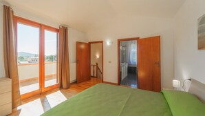 Ein Schlafzimmer mit einem großen Bett, einem Kleiderschrank, einem Badezimmer mit Dusche und einem Balkon mit Vorhängen.