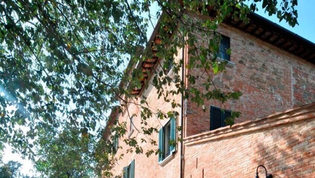 Un área de comedor al aire libre con mantel a cuadros rojo y blanco, diversos alimentos y un edificio de ladrillo rústico al fondo.