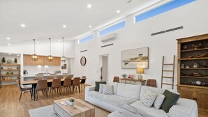 A spacious living area with a dining table, a sofa, and a coffee table. There are multiple chairs, a clock, and a painting on the wall. - Bella Beach Resort - An Oasis on the Bellarine (Saint Leonards)