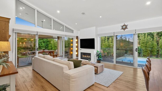 A spacious living room with a large sofa, a fireplace, and a TV. There is a sliding glass door leading to a pool area. - Bella Beach Resort - An Oasis on the Bellarine (Saint Leonards)