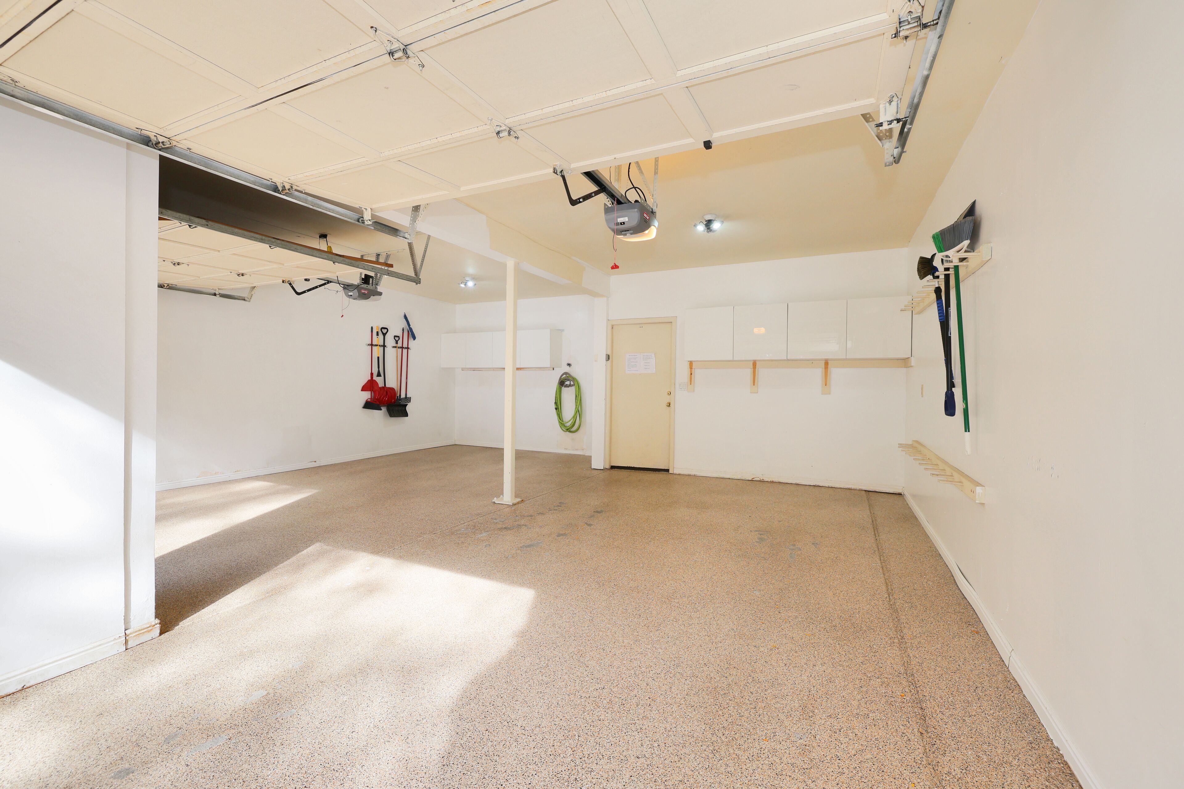 Una stanza spaziosa con soffitto alto, una porta e un appendiabiti a parete con attrezzi per la pulizia.