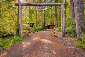 Enter the serene forest through the rustic TAMANAWAS archway, leading to a secluded cabin nestled among the trees.