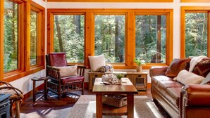 A cozy cabin interior with large windows, wooden furniture, and a view of a forest. - Magnificent Mountain Cabin on 5 Acres Next to Creek, Picturesque Outdoor Space, Hot Tub, Ping Pong (Rhododendron)