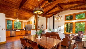 A spacious kitchen with wooden cabinets, a stainless steel refrigerator, and a dining area with a wooden table and leather chairs. - Magnificent Mountain Cabin on 5 Acres Next to Creek, Picturesque Outdoor Space, Hot Tub, Ping Pong (Rhododendron)