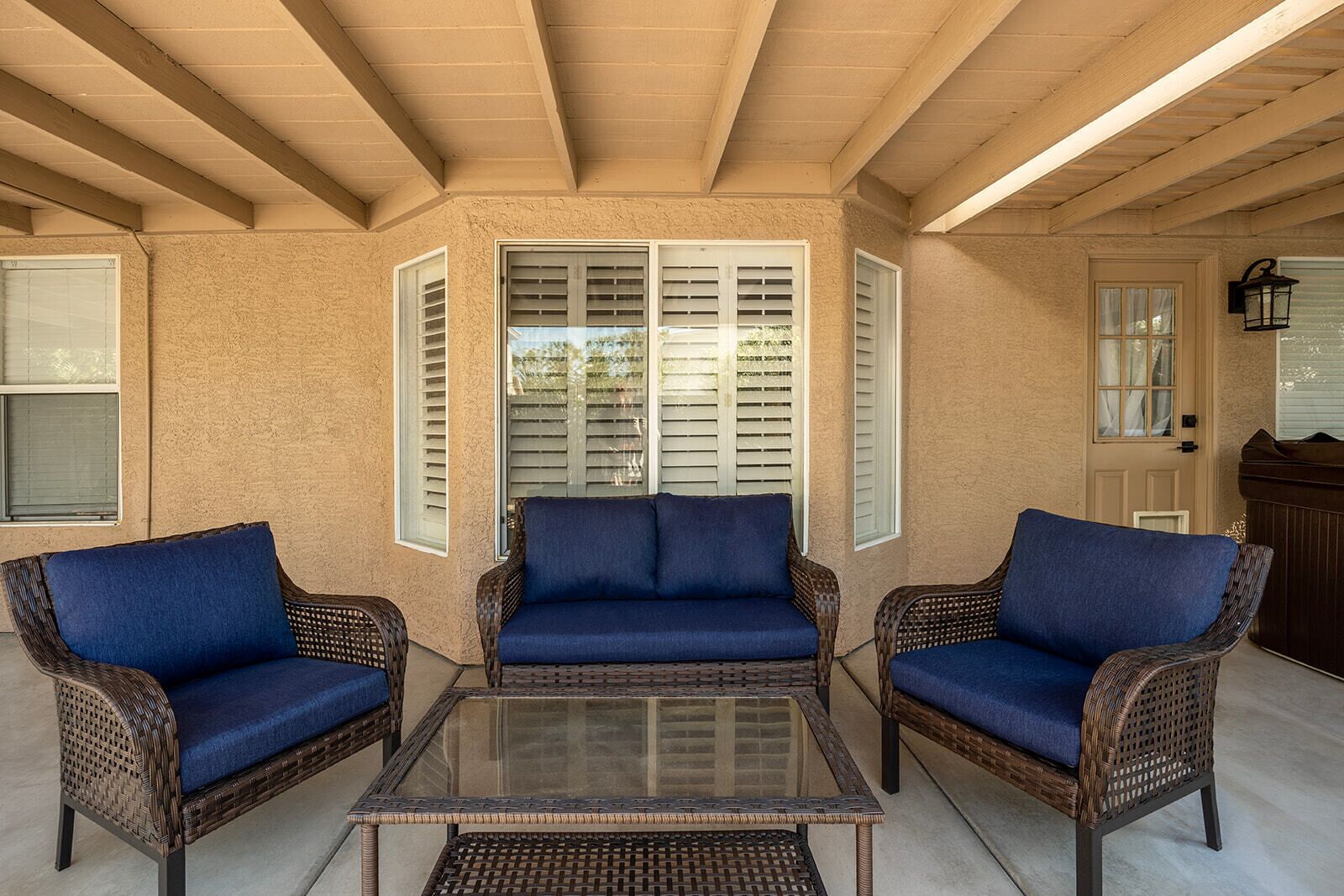 A covered patio area with wicker furniture and a glass table.