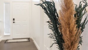 En hall med en hög vas med pampasgräs på höger sida, vita väggar och en dörr längst ner.
