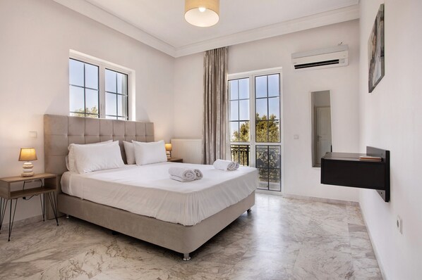 A modern bedroom with a large bed, two bedside tables, a wall-mounted air conditioning unit, and a balcony view.