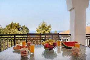 A table with breakfast items, including croissants, fruit, and drinks, on a balcony with a view.