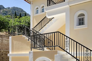 A building with a beige exterior, a staircase with black railings, and a view of a mountainous landscape.