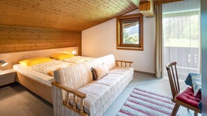 A cozy bedroom with a wooden ceiling, a bed with yellow pillows, a striped sofa, and a view of a mountainous landscape through a window. - Spacious holiday apartment in Aschau (Aschau im Zillertal)