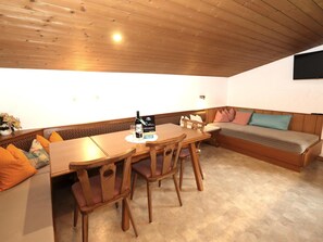 Ein gemütliches Zimmer mit einem Holzespeisetisch und -stühlen, einer Couch mit Kissen sowie einem wandmontierten Flachbildfernseher.