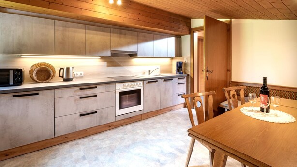 A modern kitchen with wooden cabinets, a built-in oven, and a dining area with a wooden table and chairs. - Spacious holiday apartment in Aschau (Aschau im Zillertal)