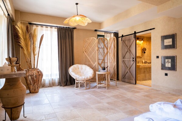 A room with a large window, a chair, a table, and a door leading to another room. - Bi Ada Otelleri (Bozcaada)