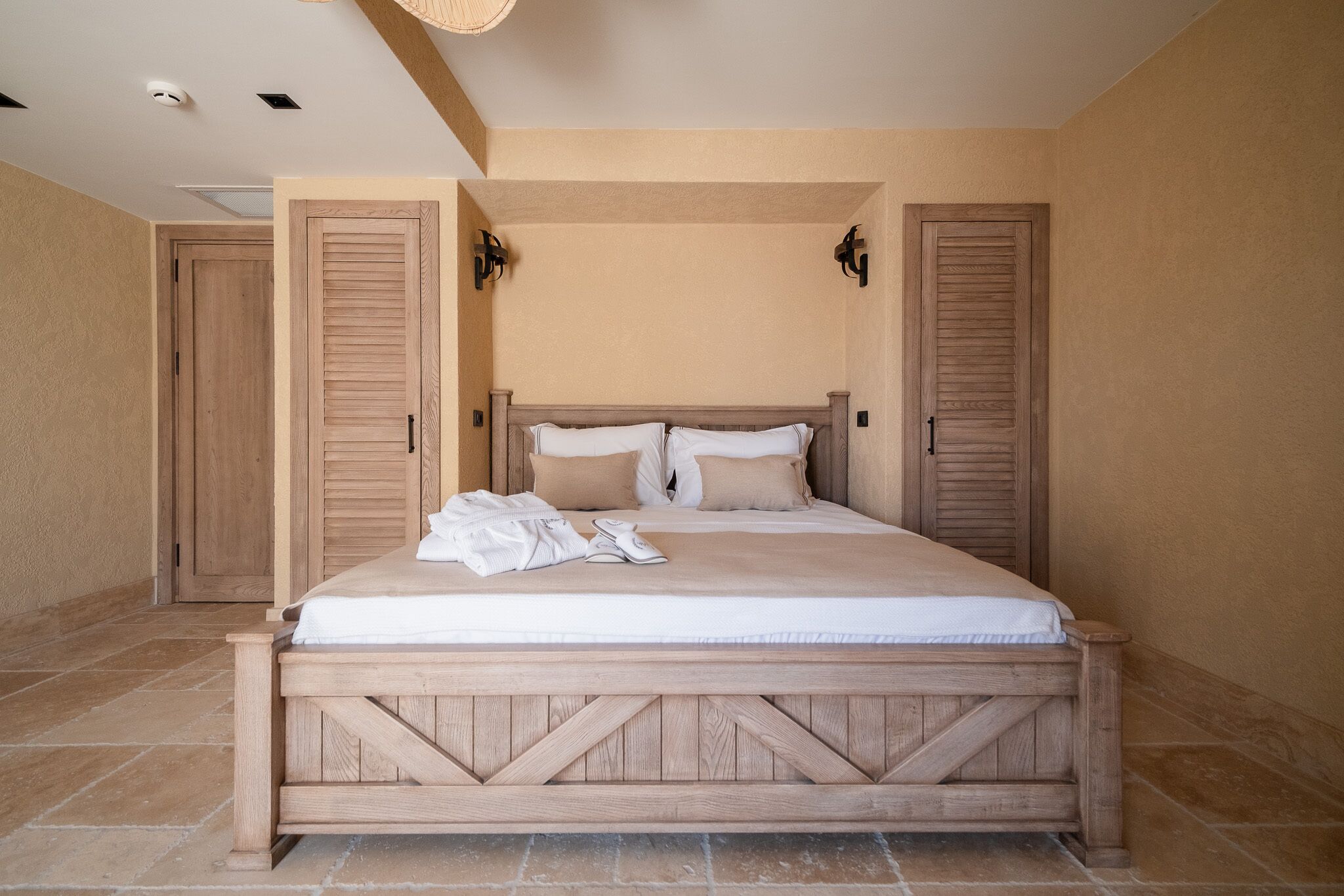 A bedroom with a wooden bed frame, two doors, and a light fixture above the bed.