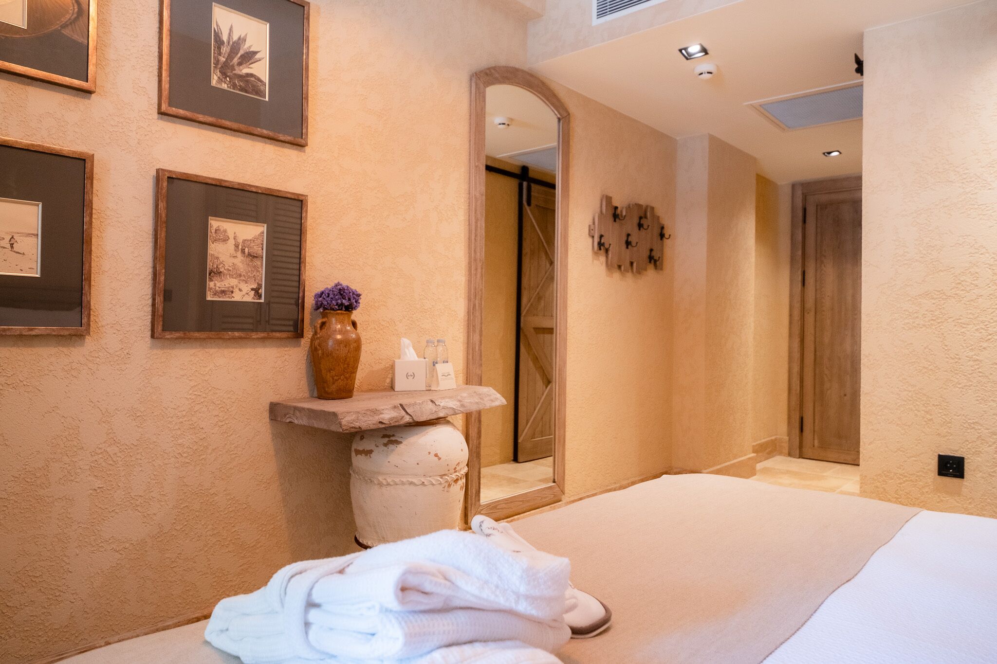 Een hotelkamer met een groot bed, een kaptafel met spiegel, ingelijste foto’s aan de muur en een kleine vaas met bloemen.
