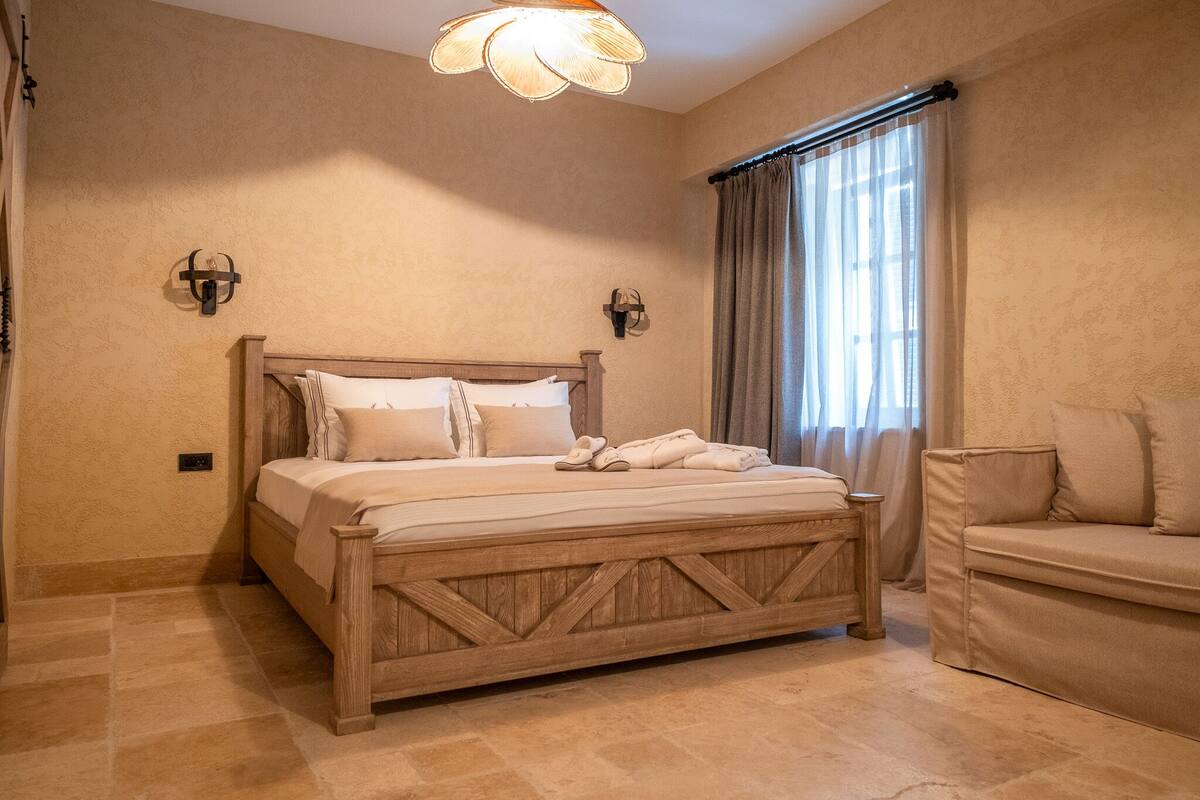 A bedroom with a wooden bed, a beige sofa, and a large window with curtains.