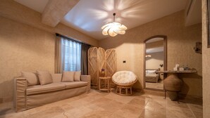 Una habitación con un sofá color beige, un sillón redondo de mimbre, un espejo grande y una lámpara decorativa en el techo.