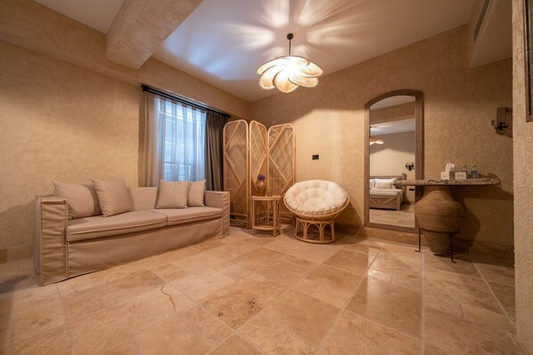 A room with a beige sofa, a round wicker chair, a large mirror, and a decorative ceiling light. - Bi Ada Otelleri (Bozcaada)