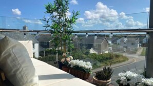 Ein Balkon mit einer weißen Couch, Blumentöpfen und Blick auf eine Wohnstraße.