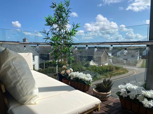 A balcony with a white sofa, potted plants, and a view of a residential street. - Boho-Chic Apartment with Sea Views & Parking (Newquay)