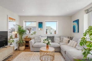 A modern living room with a sectional sofa, a TV, and various plants. - Boho-Chic Apartment with Sea Views & Parking (Newquay)