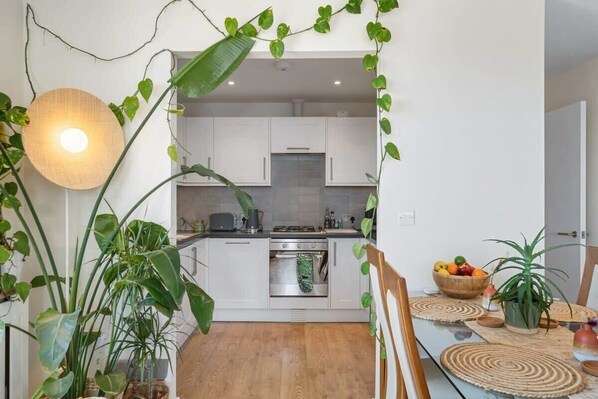 A modern kitchen with white cabinets, a built-in oven, and a dining area with a wooden table and chairs.