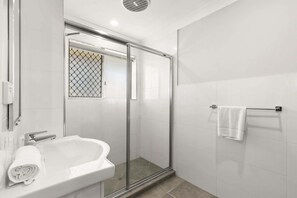 A modern bathroom with a glass shower enclosure, a white sink, and a towel rack.