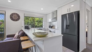 Une cuisine moderne dotée d’un grand îlot central, d’un réfrigérateur noir et d’un coin repas avec un canapé et des tabourets de bar.