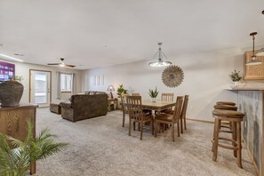 A spacious living room with a sofa, a dining table with chairs, and a ceiling fan.