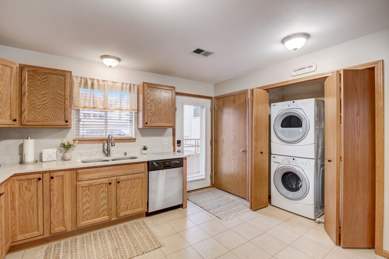 A kitchen with wooden cabinets, a dishwasher, a sink, and a double washing machine.