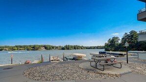 Un espace de pique-nique au bord du lac, équipé d’un barbecue, d’une table de pique-nique et de plusieurs bateaux amarrés à proximité.