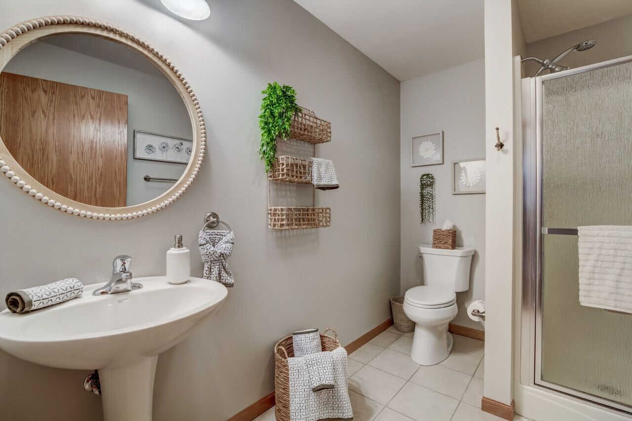 A bathroom with a round mirror, a sink, a toilet, and a shower area.