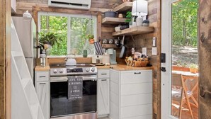Een compacte keuken met houten wanden, een inbouwoven en een raam met uitzicht op groen.