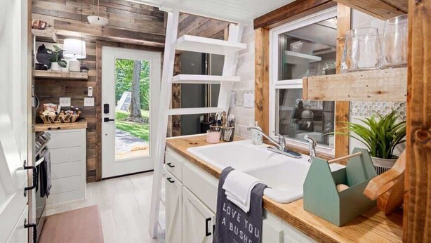 Een moderne keuken met witte kasten, een houten aanrechtblad en een raam met uitzicht op een tuin.
