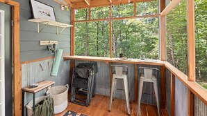 Een chalet met houten inrichting, een groot raam met uitzicht op een bos, een kleine tafel en een stoel.