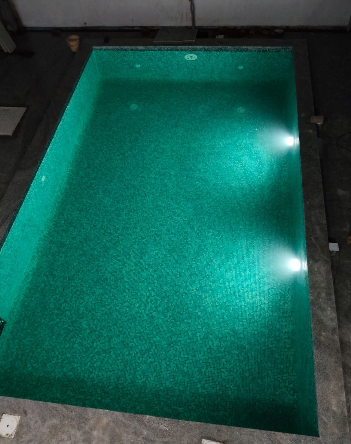 Une piscine d’eau verte à la surface texturée, entourée d’une terrasse en béton.