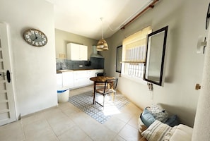 A compact kitchen with a dining area, a clock, and a window with blinds.