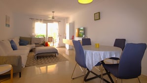 A living room with a sofa, a dining table with chairs, a ceiling fan, and a window with curtains. - Golden - Javea, Costa Blanca (Javea)