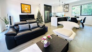 Una sala de estar moderna con un sofá de cuero negro, una mesa de centro blanca y un árbol de Navidad.